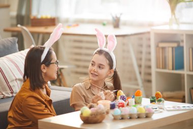 Girl painting eggs with mother