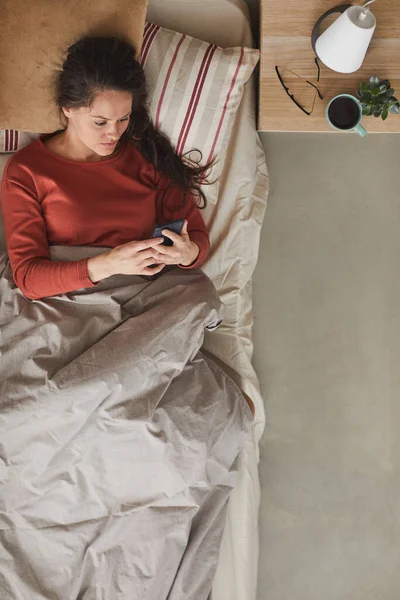 Mujer con teléfono en la cama — Foto de Stock