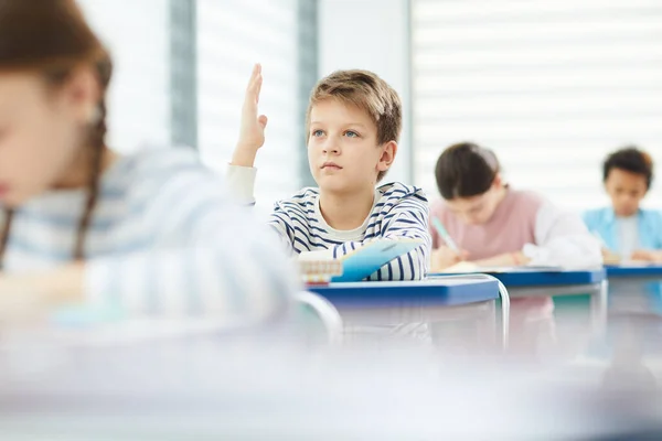 Rapaz inteligente levantando a mão na classe — Fotografia de Stock