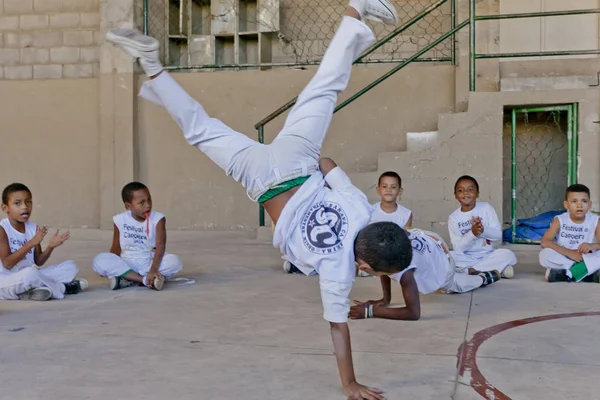 Rio de Janeiro, Brezilya - 9 Ağustos 2016: Brezilya 'da Capoeira sınıfındaki çocuklar Berimbau oynayan bir öğretmenle arka planda bir gecekondu mahallesindeki açık hava spor sahasında arkadaşlarıyla çember oluşturuyorlar.