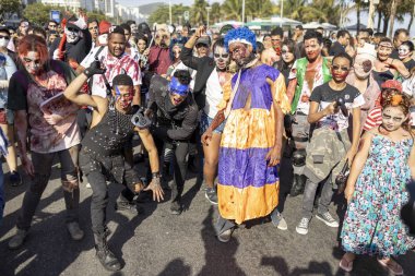 Rio de Janeiro, Brezilya - 2 Kasım 2019: Cadılar Bayramı Zombi Yürüyüşü kalabalık Ölüler Günü 'nde Copacabana Bulvarı' nda güneşli bir günde arka planda palmiye ağaçları ile ilerliyor.