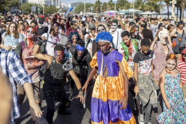 Rio de Janeiro, Brezilya - 2 Kasım 2019: Cadılar Bayramı Zombi Yürüyüşü kalabalık Ölüler Günü 'nde Copacabana Bulvarı' nda güneşli bir günde arka planda palmiye ağaçları ile ilerliyor.