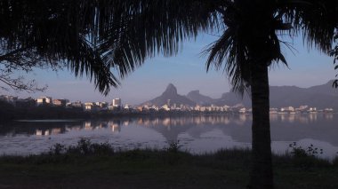 Şehir gölünün ön planında palmiye ağaçlarının silueti ve arka plandaki suda yansıması da dahil olmak üzere iki kardeş dağının hava manzarası.