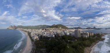 Rio de Janeiro 'nun geniş hava manzarası Arpoador kayasından ön planda Ipanema ve Copacabana plajları ve arka planda bulutlu bir gökyüzüne karşı daha geniş şehir manzarası.
