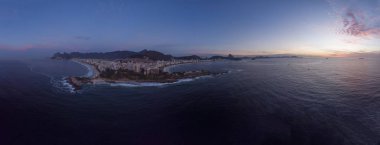 Rio de Janeiro 'nun önde Arpoador kayası, Ipanema ve Copacabana plajlı geniş panorama ve gün doğumunda mavi saatte arka planda daha geniş şehir manzarası