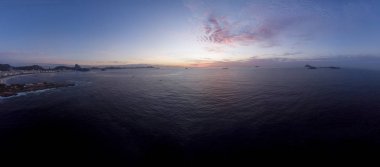Rio de Janeiro 'daki Arpoador Şeytan Sahili' nden mavi saat güneş doğar. Arka planda Copacabana kalesi ve Sugarloaf dağı bulunur. 