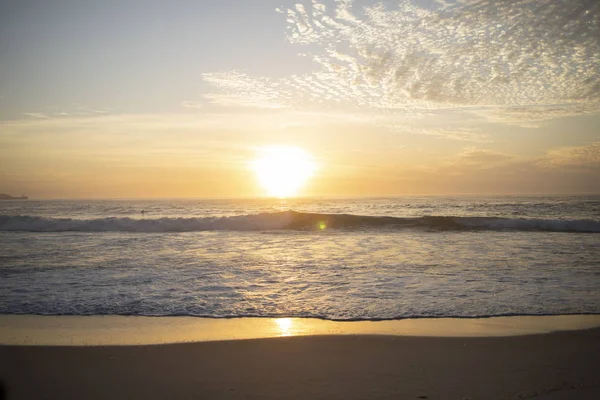 在巴西里约热内卢的Arpoador魔鬼海滩上 深橙色的波浪涌来 日出时分 阳光反射在水面上 映入原始的沙滩上 免版税图库照片