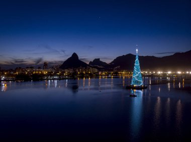 Gün batımında Rio de Janeiro gölünün ortasında çelenklerle birlikte yüzen Noel ağacının ışıkları.