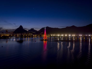 Gün batımında Rio de Janeiro gölünün ortasındaki yüzen Noel ağacının ışıkları kırmızı renkte.