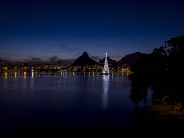 Günbatımında Rio de Janeiro gölünün ortasındaki yüzen Noel ağacının ışıkları beyaz renk düzeniyle