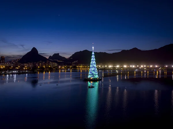 Gün batımında Rio de Janeiro gölünün ortasındaki yüzen Noel ağacının ışıkları mavi renkte.