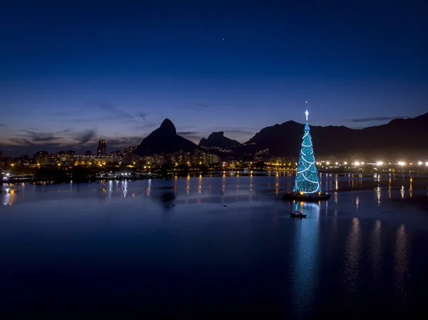 Gün batımında Rio de Janeiro gölünün ortasında çelenklerle birlikte yüzen Noel ağacının ışıkları.