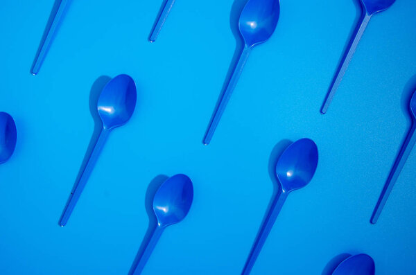 Pattern of blue plastic spoons on blue background. Blue color of 2020 year. Colorful pop pattern