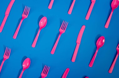 Renkli arka planda duran pembe plastik tek kullanımlık çatalların, kaşıkların ve bıçakların derisi yüzülmüş. Yaratıcı üst görünüm deseni.