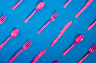 Renkli arka planda duran pembe plastik tek kullanımlık çatalların, kaşıkların ve bıçakların derisi yüzülmüş. Yaratıcı üst görünüm deseni.