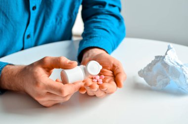 Evde elinde haplarla bir kavanoz tutan genç bir adamın fotoğrafı. Gerçek problem, soğuk ve soğuk, tıbbi tasarım için arka plan