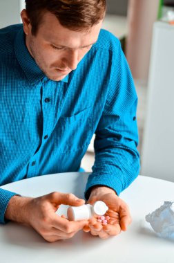 Evde elinde haplarla bir kavanoz tutan genç bir adamın fotoğrafı. Gerçek problem, soğuk ve soğuk, tıbbi tasarım için arka plan