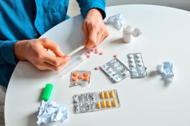 Evde termometre ve bir sürü hap tutan genç bir adamın fotoğrafı. Gerçek problem, soğuk ve soğuk, tıbbi tasarım için arka plan