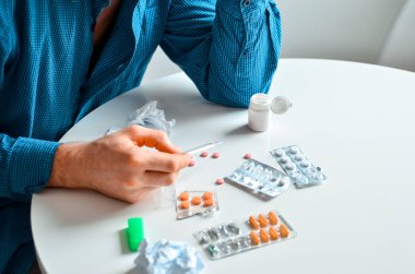 Evde termometre ve bir sürü hap tutan genç bir adamın fotoğrafı. Gerçek problem, soğuk ve soğuk, tıbbi tasarım için arka plan