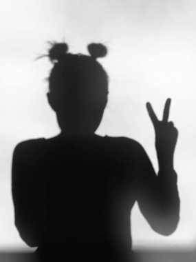 Profilde beyaz bir duvara dayanmış genç bir kadının gölgesi. Duvardaki kadın silueti