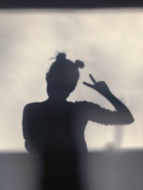 Profilde beyaz bir duvara dayanmış genç bir kadının gölgesi. Duvardaki kadın silueti