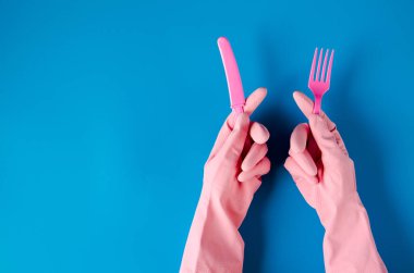 Pembe temizleme eldivenleri, pembe bıçaklı ve çatallı mavi arka plan. Virüsten korunuyor, metin için boşluk