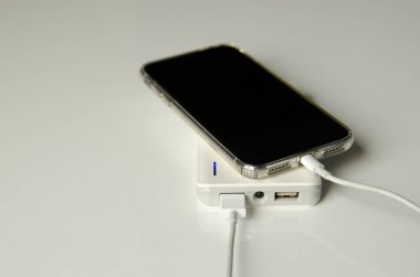 Beyaz arka planda izole edilmiş elektrik bankasıyla akıllı telefon şarjı çekimleri. Cep telefonu şarj ediliyor