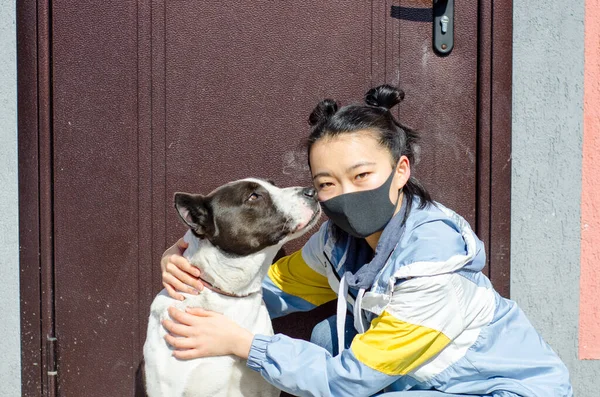 Young korean girl in protective face mask looking at dog wearing medical mask too. Chinese Coronavirus disease COVID-19 is dangerous for pets concept