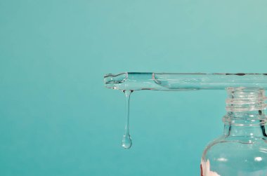 Pipetten şişeye yağ damlıyor. Esans sıvı kozmetik. Şurup. Parfüm. Romaterapi. Mavi naneli arkaplanda izole edilmiş