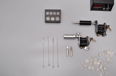 Dövme makineleri, iğneler ve gri arka planda izole edilmiş tüm bu dövme şeyleri. Dövme silahları. Dövme makineli desen, iş tasarımınız için duvar kağıdı