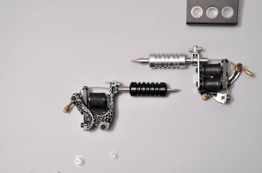 Dövme makineleri, iğneler ve gri arka planda izole edilmiş tüm bu dövme şeyleri. Dövme silahları. Dövme makineli desen, iş tasarımınız için duvar kağıdı