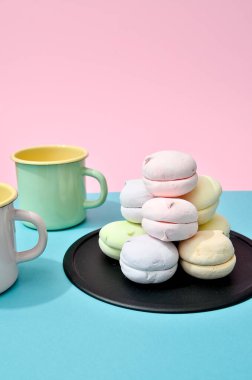 Tabaktaki pastel renkli marşmelov manzarası ve pastel renkli pembe arka planda iki boş kupa. Minimalizm tarzı.