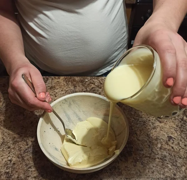 Kobieta cukiernik wylewać skondensowane mleko do miski — Zdjęcie stockowe