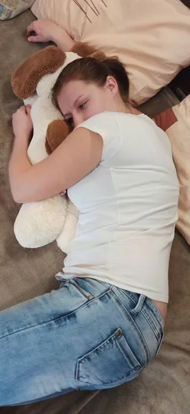 Frau liegt auf Bett und umarmt Teddyhund — Stockfoto