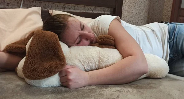 Woman sleeping on bed and hugging teddy dog