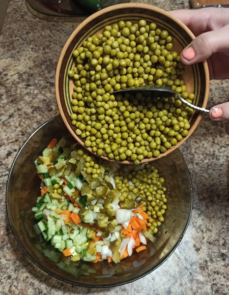 Woman cook pour peas to bowl with vegetables — Stock Photo, Image