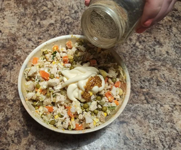 Mulher cozinheiro despeje pimenta preta para tigela com salada — Fotografia de Stock