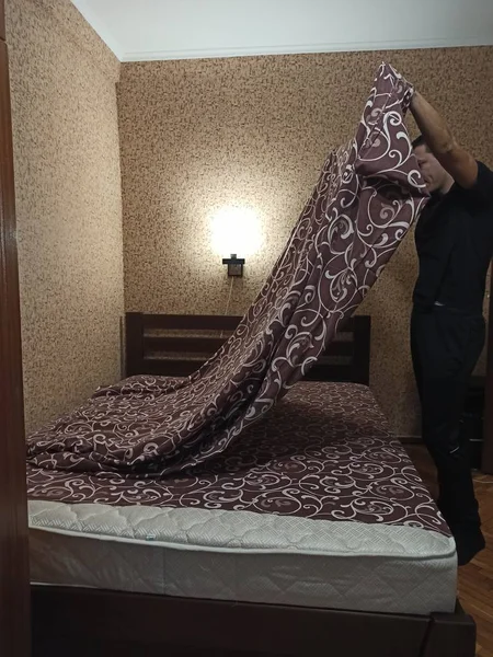 European man hold duvet cover over bed in bedroom