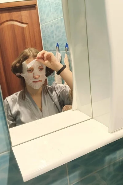 Kobieta patrzy w lustro na twarz z maską na twarzy — Zdjęcie stockowe