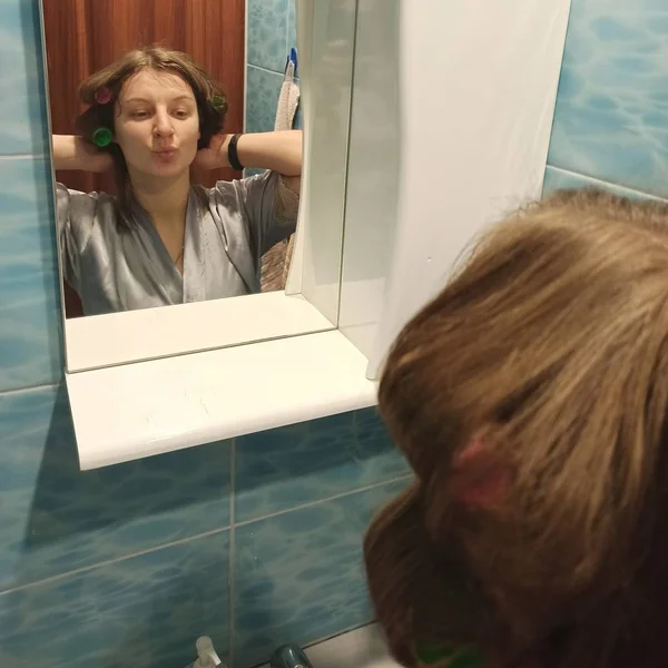Женщина с бигуди в волосах смотрится в зеркало — стоковое фото
