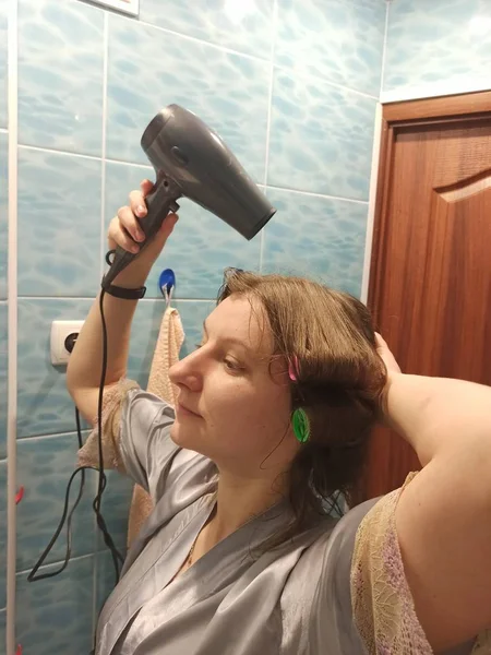 European woman dry hair with hairdryer at bathroom