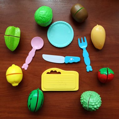 Toy cutleries and fruits on wooden background