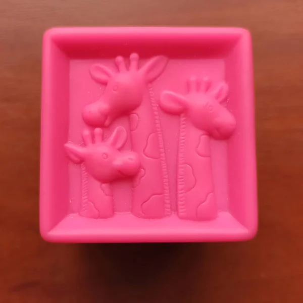 Pink toy cube with giraffes on wooden background