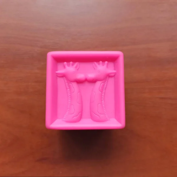 Pink toy cube with giraffes on wooden background