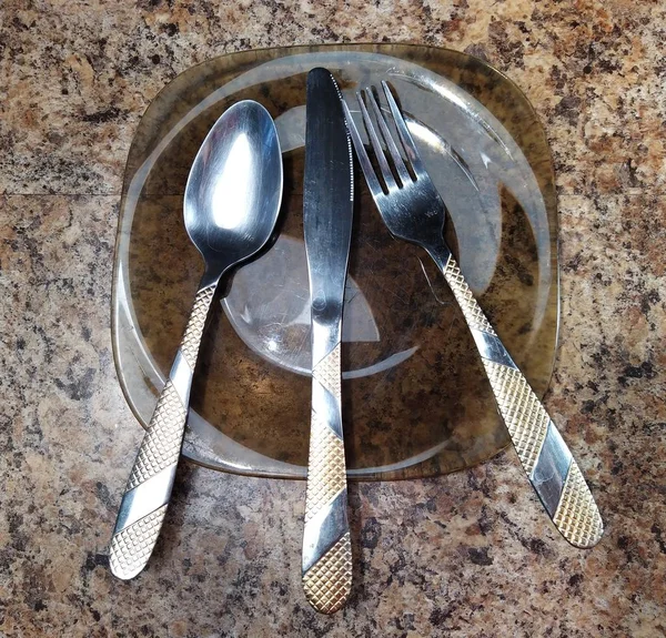 Talíř s lžící, vidličkou a nožem na kuchyňském stole — Stock fotografie