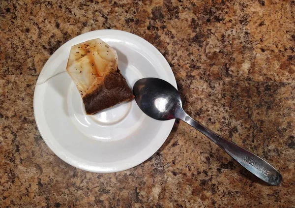 Piatto con cucchiaino e bustina di tè su sfondo tavolo da cucina — Foto Stock