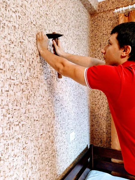 European man nails nail on wall in bedroom at home