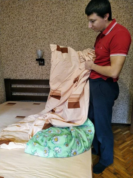 European man hold duvet cover over bed in bedroom