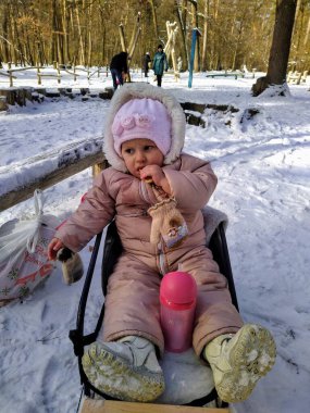 Avrupalı küçük kız kızağa oturup karlı kış ormanlarında pasta yiyor.