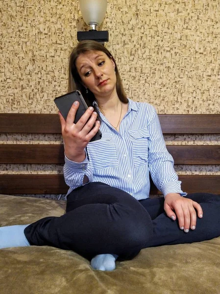Ευρωπαϊκή Γυναίκα Σκεπτικιστικό Πρόσωπο Κάθεται Στο Κρεβάτι Και Χρησιμοποιήσετε Smartphone — Φωτογραφία Αρχείου